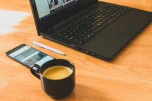 Black laptop computer beside a black ceramic tea cup on a desk.
